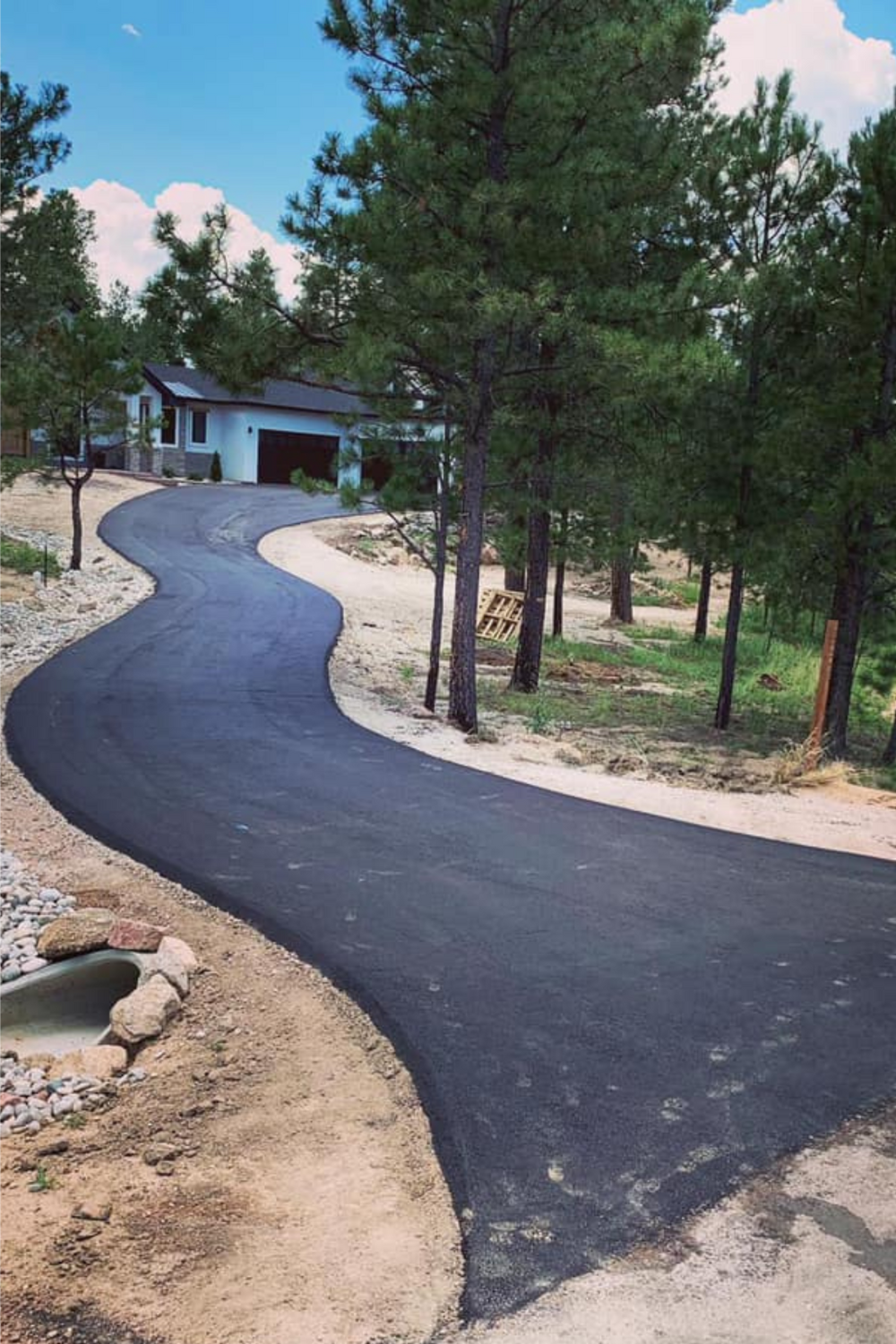New 3.5 inch hot mix asphalt S-curve driveway winding through ponderosa pines to garage at Whispering Pines Colorado Springs residence with drainage culvert by Dawley Asphalt