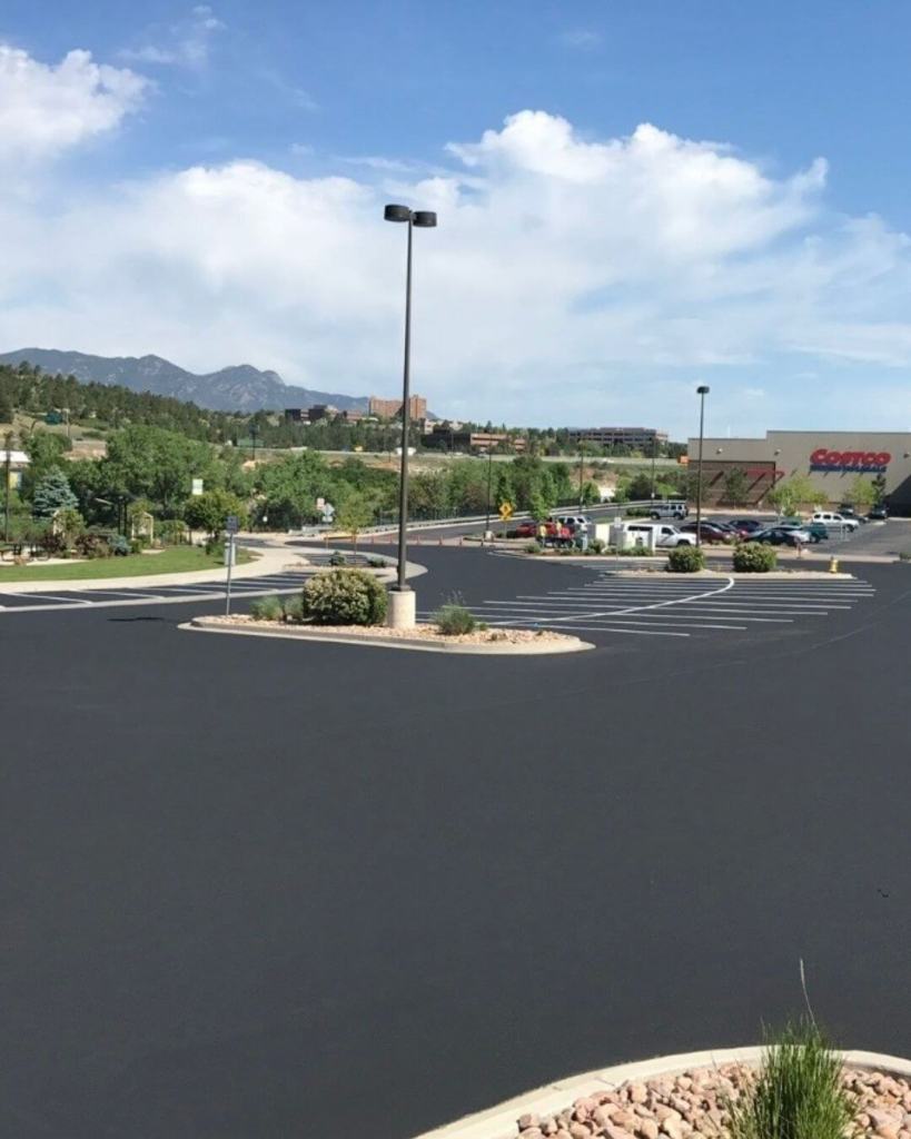 Expansive freshly crack sealed and seal coated commercial parking lot with white line striping in Colorado Springs with mountains and Costco visible in background by Dawley Asphalt