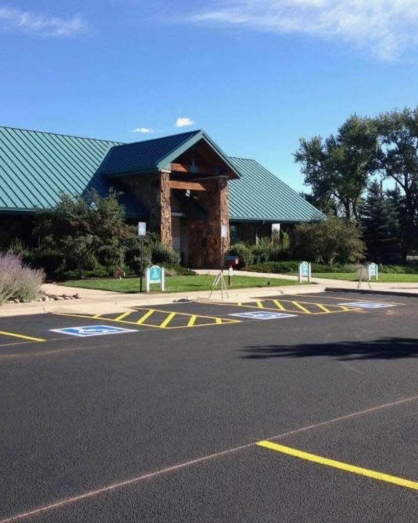 Freshly seal coated and yellow ADA striped parking lot at the Colorado Springs Humane Society by Dawley Asphalt with stone and green metal roof building entrance