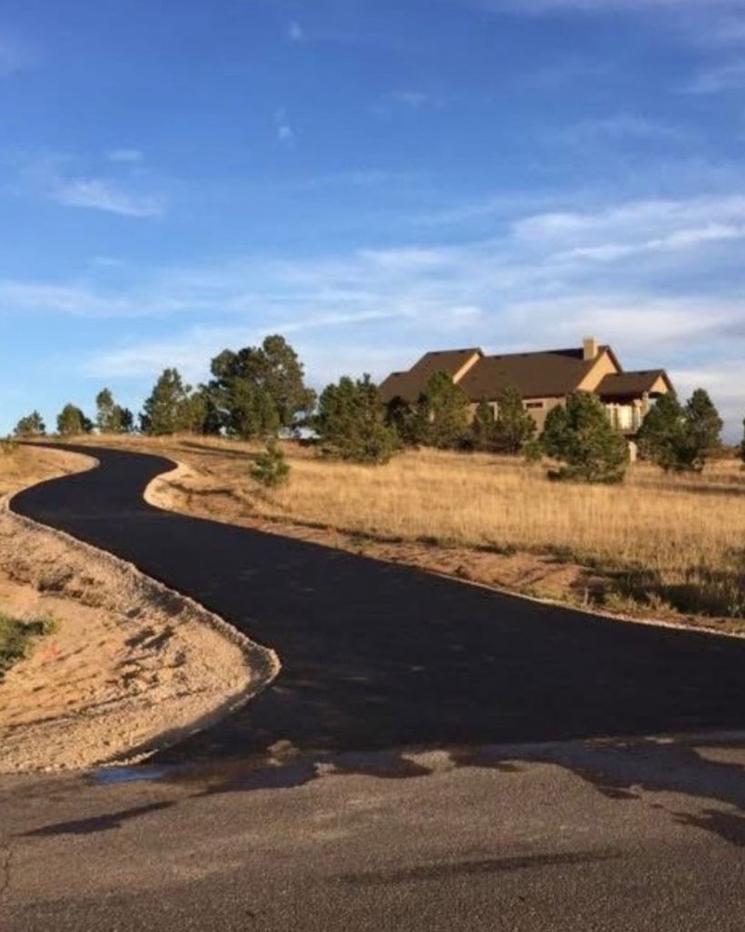 New 3.5 inch hot mix asphalt curved driveway across open golden grassland leading to ranch style home in Black Forest Colorado Springs by Dawley Asphalt