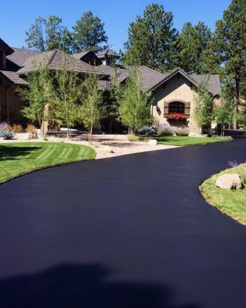 Hand applied seal coat on wide curved estate driveway with manicured lawn stone home and flower window boxes at Cathedral Pines Colorado Springs by Dawley Asphalt