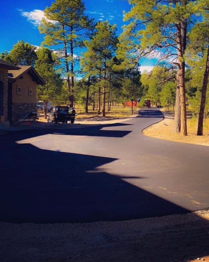 New 3.5 inch hot mix asphalt wide driveway and turnaround installation on pine shaded Black Forest Colorado Springs residential lot with vivid blue sky by Dawley Asphalt
