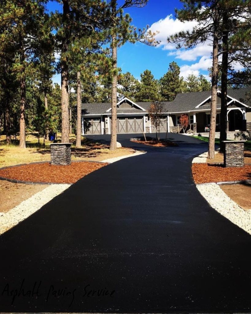 Hand applied seal coat on residential driveway garage approach at High Forest Ranch Colorado Springs craftsman home with ponderosa pines and mulched landscape beds by Dawley Asphalt