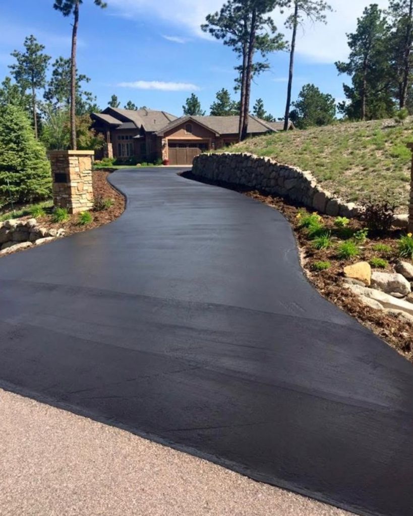 Hand applied seal coat on winding private estate driveway with stone pillars and boulder retaining wall in Cathedral Pines Colorado Springs by Dawley Asphalt
